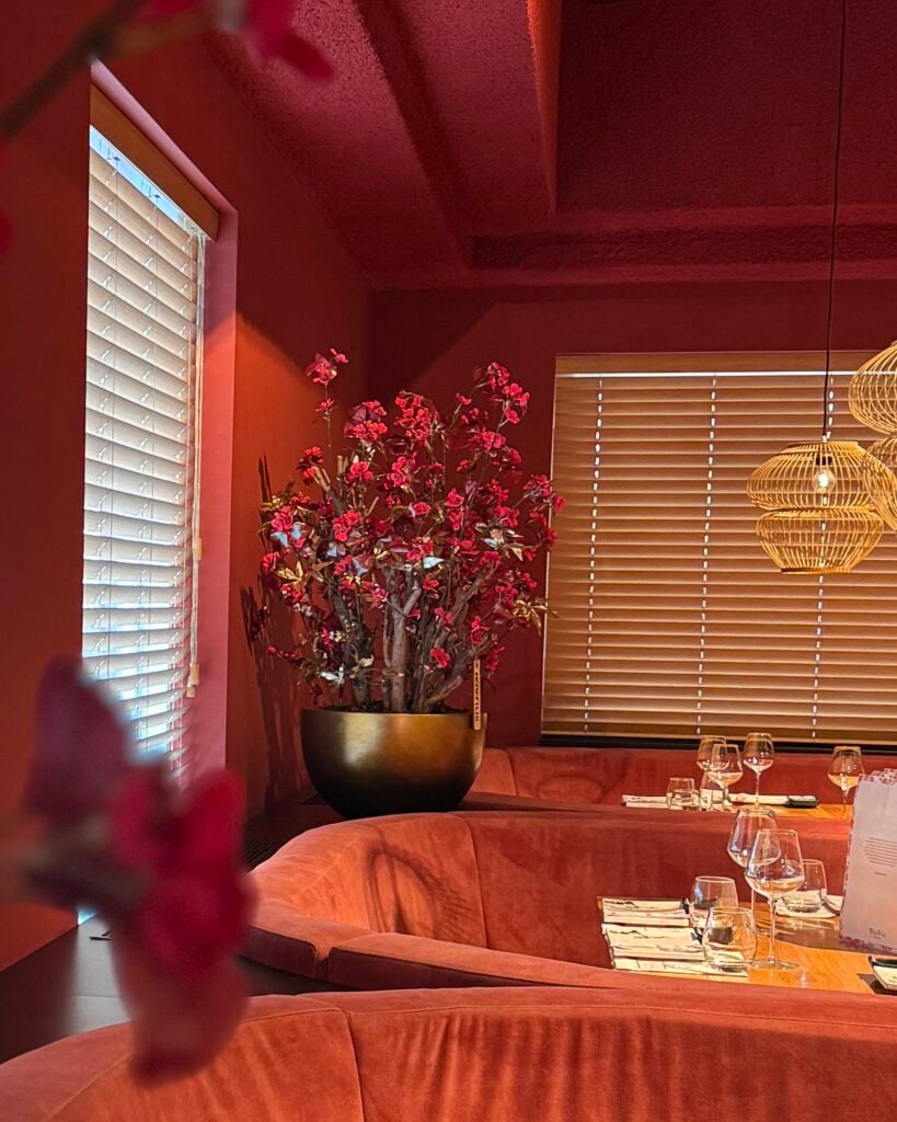 zijden bloemstuk SUSU met rode bloesem en goud blad in luxe pot, geplaatst in warm restaurantinterieur STYLERZ24