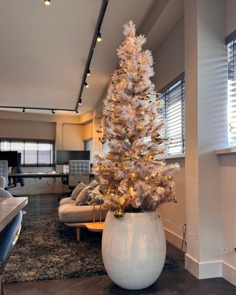 Luxe kunst kerstboom van 200 cm in beige-goud met warmwitte verlichting en gouden ballen, geplaatst in een moderne witte pot in een stijlvol kantoorinterieur. STYLERZ24