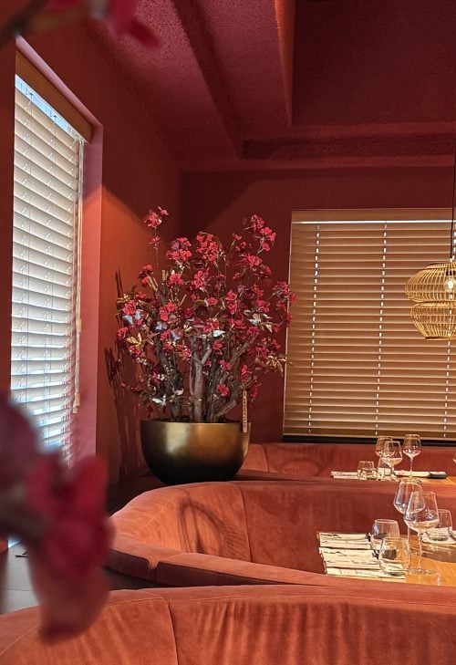 zijden bloemstuk SUSU met rode bloesem en goud blad in luxe pot, geplaatst in warm restaurantinterieur STYLERZ24